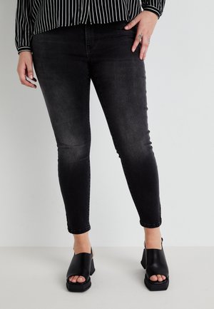 Black skinny jeans made of denim, featuring a faded finish and ankle length. Paired with black open-toed heeled sandals.