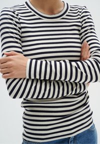 Haut à manches longues c ôtelé avec des rayures bleu marine et blanches, doté d'un col rond et d'une coupe ajustée. Le tissu présente une apparence texturée.