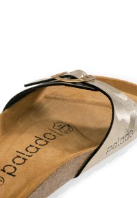 Sandal in metallo argentato con cinturini neri di accento, una soletta in sughero testurizzato e un dettaglio in metallo dorato sulla cinghia.