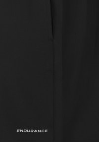 Sorte atletiske shorts med en glat tekstur, detaljeret syning, en lynlåslomme og "ENDURANCE" logo i hvid på forsiden.