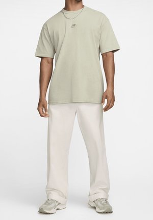 Lys grøn bomulds T-shirt med korte ærmer og et lille Nike-logo, parret med løse hvide bukser og grå sneakers.