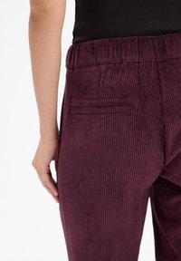 Lila Kordhose mit vertikalen Streifen, ausgestattet mit einem elastischen Bund und einer einzelnen Gesäßtasche. Glatte Textur, figurbetonte Silhouette.