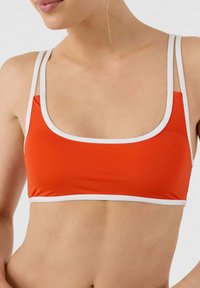 Soutien-gorge de sport rouge avec des finitions blanches, doté d'un décolleté carré et de bretelles fines, fabriqué en tissu extensible, conçu pour le confort.
