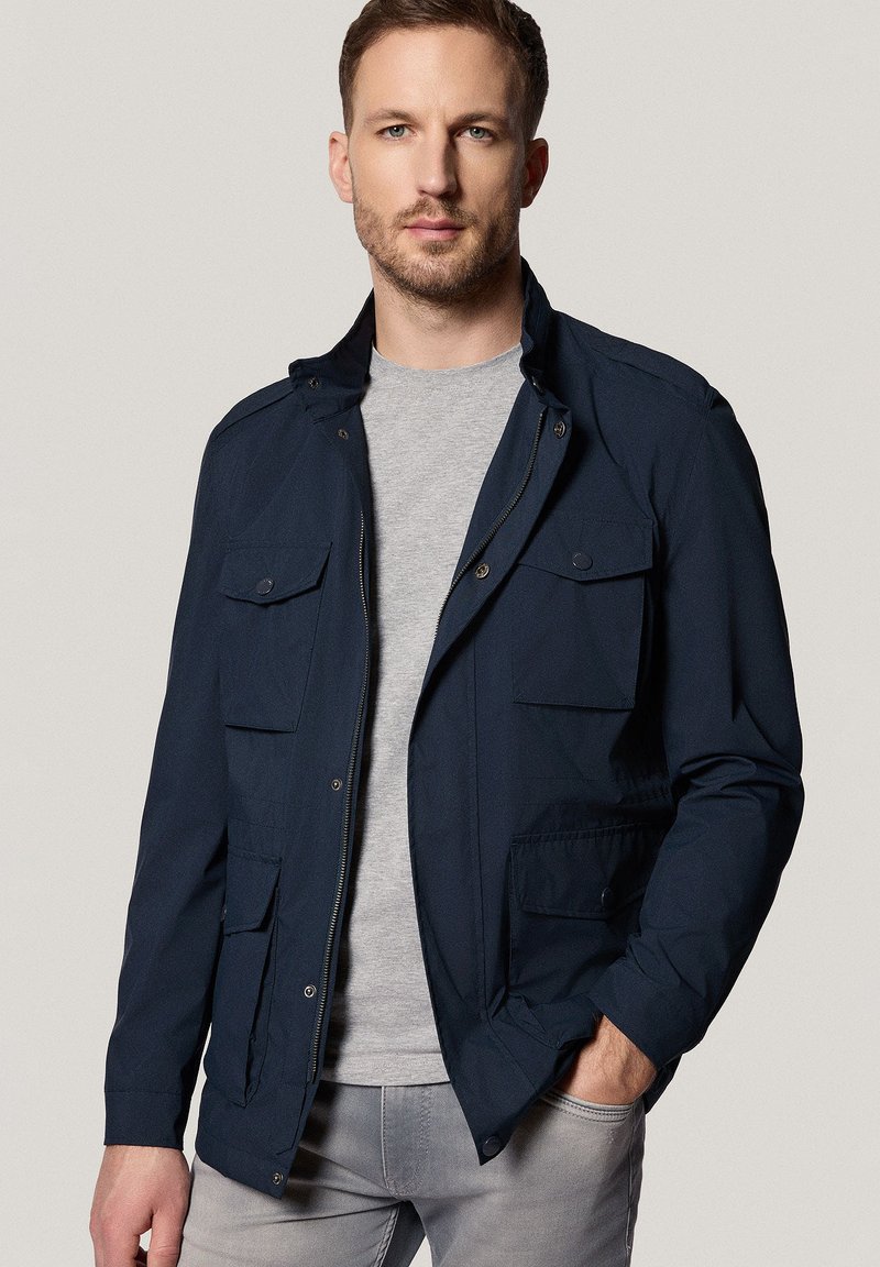 Granatowa kurtka z zamkiem błyskawicznym i zapięciem na napy, z dwoma kieszeniami na piersi i bocznymi, zaprojektowana z lekkiego materiału i w klasycznym fasonie.