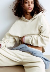 Crème hoodie met een oversized pasvorm en een v-hals capuchon, gecombineerd met lichtblauwe broek met een tailleband. Soepele textuur, casual ontwerp, ontspannen silhouet.