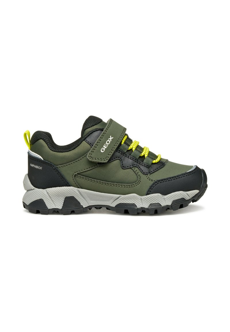 Chaussure de sport verte et noire avec un extérieur texturé, des lacets élastiques, une sangle Velcro et une semelle gris robuste avec un motif de traction noir.