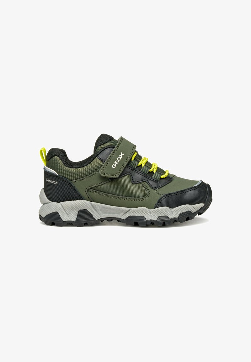 Zapatilla deportiva verde y negra con un exterior texturizado, cordones elásticos, correa de Velcro y una suela gris resistente con tacos negros.
