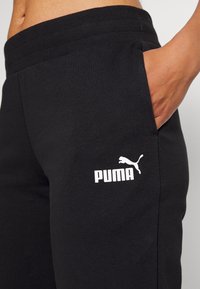 Black sweatpants featuring a textured waistband, side pocket, and white Puma logo on the thigh. Made of soft cotton blend fabric.