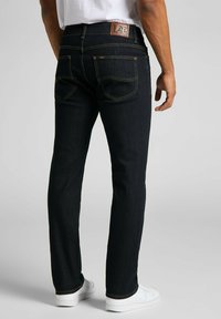 Jeans de mezclilla azul oscuro con corte recto y costuras amarillas contrastantes. Presenta una etiqueta de logo de cuero en la parte trasera de la cintura y dos bolsillos traseros.