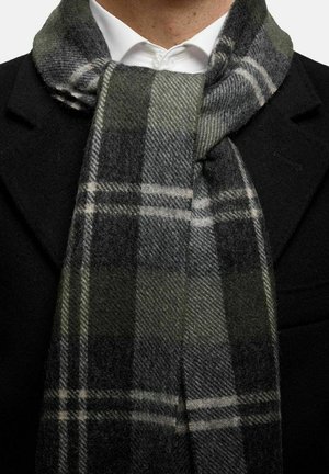 Ullscarf i grön och grå rutmönster, med en mjuk textur som hänger kring kragen, mot en bakgrund av en svart kappa.
