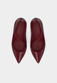 Ζευγάρι γυαλιστερές σκουροκόκκινες επίπεδες παπούτσια με μυτερή μύτη και χρυσό λογότυπο Tommy Hilfiger στο εσωτερικό και εξωτερικό άκρο.