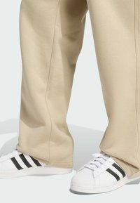 Beżowe dresy o luźnym kroju i szczegółach bocznych, połączone z białymi sneakersami z czarnymi paskami i teksturowanym noskiem.