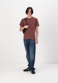 Tricou din bumbac maron cu mâneci scurte, asortat cu blugi albaștri. Geantă crossbody neagră, teniși negri cu accente albe. Design simplu.