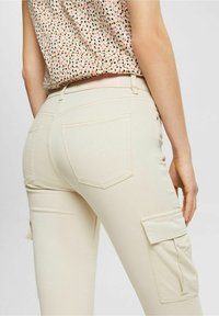 Beige cargobroek met twee zijzakken en twee achterzakken, gemaakt van een zachte, lichte stof met een gladde textuur.