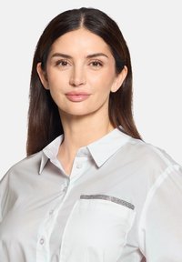 White button-up shirt with a structured collar and a shiny black rhinestone-accented pocket. Smooth texture, tailored fit, and short sleeves.