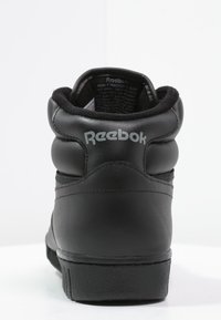 Baskets montantes noires en cuir lisse, avec un col rembourré et une semelle en caoutchouc texturée. Présente le logo "Reebok" gris à l'arrière.