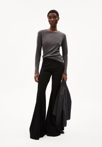 Graues Langarmoberteil, taillierte Passform. Schwarze, ausgestellte Hose mit Nahtdetails. Graue Strickjacke über dem linken Arm drapiert. Glatte, weiche Stofftexturen.