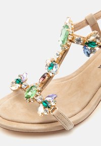 Μπεζ σανδάλι με πολύχρωμες μεγάλες και μικρές διακοσμήσεις από πολύτιμους λίθους σε λεπτά λουράκια και επένδυση με μαλακό πέλμα.