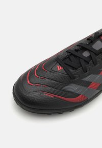 Scarpa da calcio nera con materiale testurizzato, accenti rossi e grigi, intricato design ondulato, con laccio frontale e rete traspirante.
