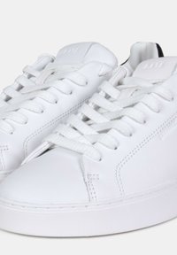 Sneaker in pelle bianca con punta rotonda, superficie testurizzata, lacci bianchi piatti e design minimalista. Presenta un branding discreto sul lato.