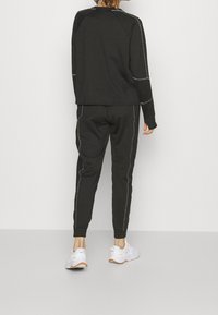 Svart atletisk outfit bestående av en långärmad topp och avsmalnande byxor med silverstickade detaljer, kombinerad med vita sneakers.