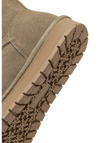 Botte en daim beige clair avec une semelle en caoutchouc texturé présentant un motif de semelle en forme de flocon de neige et un trim beige autour de la semelle.