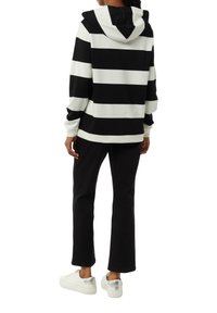 Black and white striped hoodie with a drawstring hood, cotton material, relaxed fit, worn over black pants, paired with silver-accented sneakers.