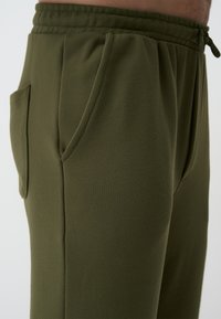 Olivgrüne Sweatpants mit einem Kordelzugbund, Seitentaschen und einer glatten Textur. Verfügt über gerafftes Material an der Taille und eine schlanke Passform.