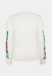 Pull blanc à manches longues avec des patches colorés à motifs abstraits courant le long des deux manches, sur un fond uni.