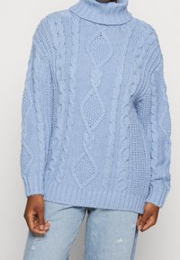 Maglione lavorato a maglia blu chiaro con colletto alto e a coste. Presenta motivi a treccia e una vestibilità rilassata. Tessuto morbido e maniche lunghe.