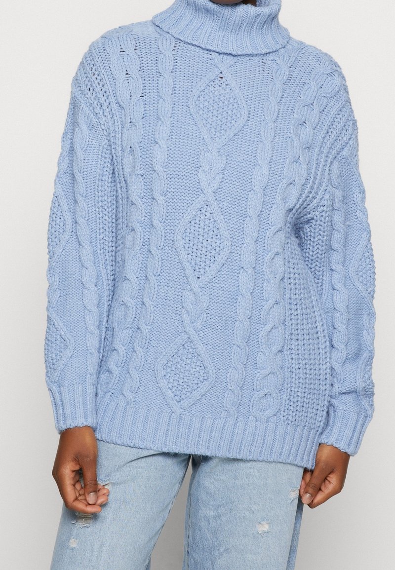 Helles blaues Strickoberteil mit hohem, geripptem Kragen. Verfügt über Zopfmuster und eine lockere Passform. Weiche Textur und lange Ärmel.