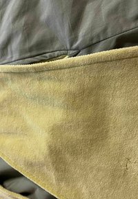 Tela verde, textura suave con un reverso amarillento y peludo, presenta una costura a lo largo del borde; el diseño es simple y funcional.