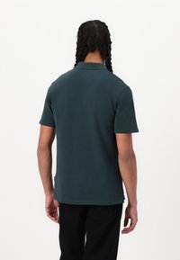Grønn kortermet polo-skjorte laget av solid stoff, med klassisk krage og en avslappet passform, med en subtil merkeetikett på siden.