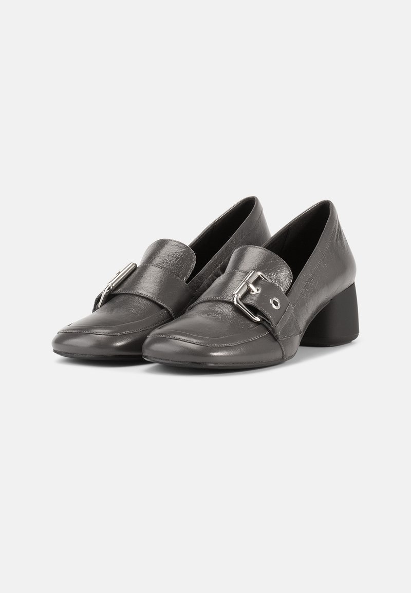 Black leather shoes with a low, block heel. Features a looped strap and silver buckle detail across the front. Smooth and textured finish.