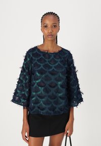 Haut bleu marine texturé avec des accents semblables à des plumes, présentant un motif en forme de coquille et des manches trois-quarts, associé à une jupe noire.
