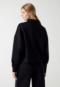 Zwarte sweatshirt met een ontspannen pasvorm, afhangende schouders en geribbelde manchetten. Het materiaal is zacht en licht gestructureerd. Verkorte lengte.