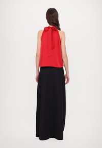 Haut sans manches rouge avec un nœud à l'arrière, associé à une longue jupe noire, texture lisse et silhouette fluide.