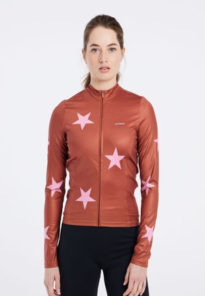 Long-sleeve zip-up top in rust with large pink star patterns. Made of a smooth, stretchy material. Features a high collar and slim fit.