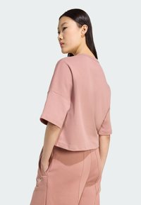 Strihaná ružová mikina vyrobená z mäkkej látky, s krátkymi rukávmi, zaobleným výstrihom a jemným logom na boku.