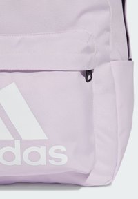 Zaino lilla realizzato in tessuto testurizzato, dotato di una tasca frontale con zip nera, grande logo Adidas bianco e spallacci imbottiti.