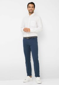 Weißes Hemd mit Knopfleiste und einer Brusttasche, kombiniert mit dunkelblauen Chinos und weißen Sneakers; glatte Stoffe, taillierte Passform.