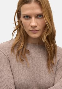 Suéter de manga larga acanalado en suave material beige con cuello redondo. Presenta una ligera textura y una silueta ajustada.