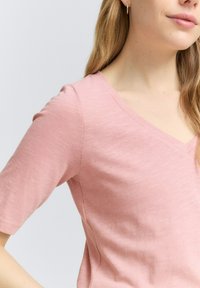 Světlá růžová V-čková trička z měkké tkaniny s krátkými rukávy. Má uvolněný střih a jemnou strukturu. Žádné výrazné vzory či akcenty.