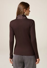 Maglietta a maniche lunghe in tessuto marrone intenso con colletto in satin liscio. Il design presenta una silhouette aderente e un minimalismo nei dettagli, abbinata a pantaloni a righe.