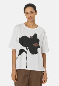 Witte katoenen T-shirt met een oversized pasvorm, voorzien van een groot zwart bloemmotief met bruine accenten. Korte mouwen en ronde halslijn.