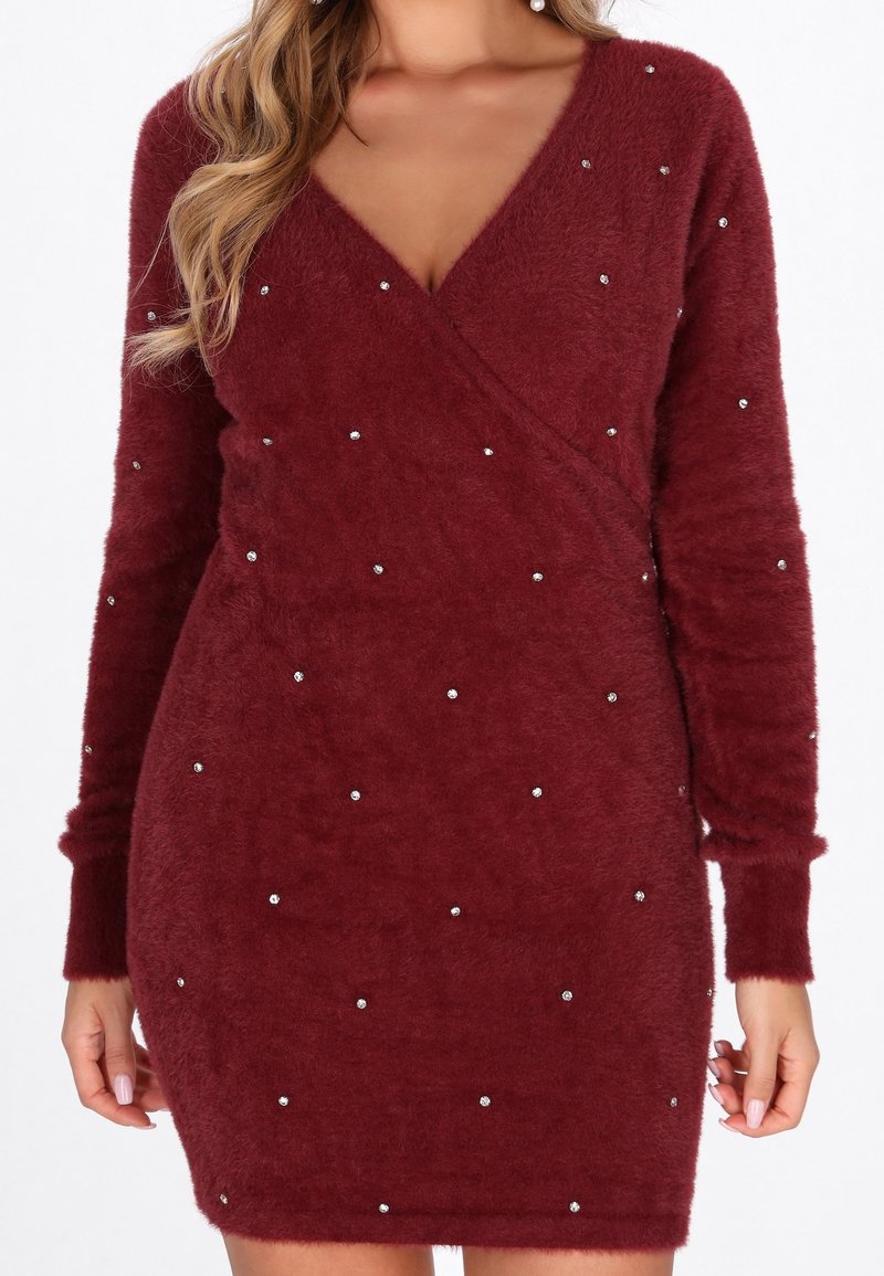 Femme portant une robe longue en tissu duveteux rouge profond à manches longues, ornée de petits strass épars et d'un décolleté en V.