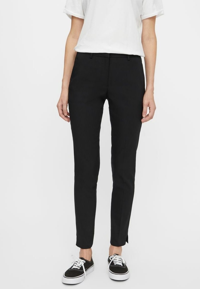 Černé slim-fit kalhoty s jemnou texturou, mají boční kapsy a diskrétní rozparek na lemu, doplněné o černé tenisky.