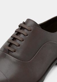 Barna bőrcipő kerek orral, hat fűzővel és sima felülettel, enyhe ívvel az oldaldizájnon.