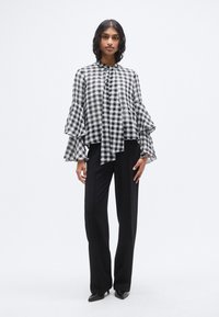 Μπλούζα με ασπρόμαυρο καρό μοτίβο, με φουσκωτά μανίκια και κορδόνι στον λαιμό, συνδυασμένη με μαύρο παντελόνι ραμμένο στα μέτρα και μαύρες μυτερές γόβες.