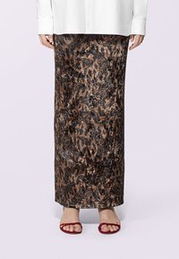 Gonna maxi a stampa leopardata in tessuto marrone e nero, caratterizzata da una texture liscia e una silhouette aderente. Indossata con sandali rossi con cinturini.